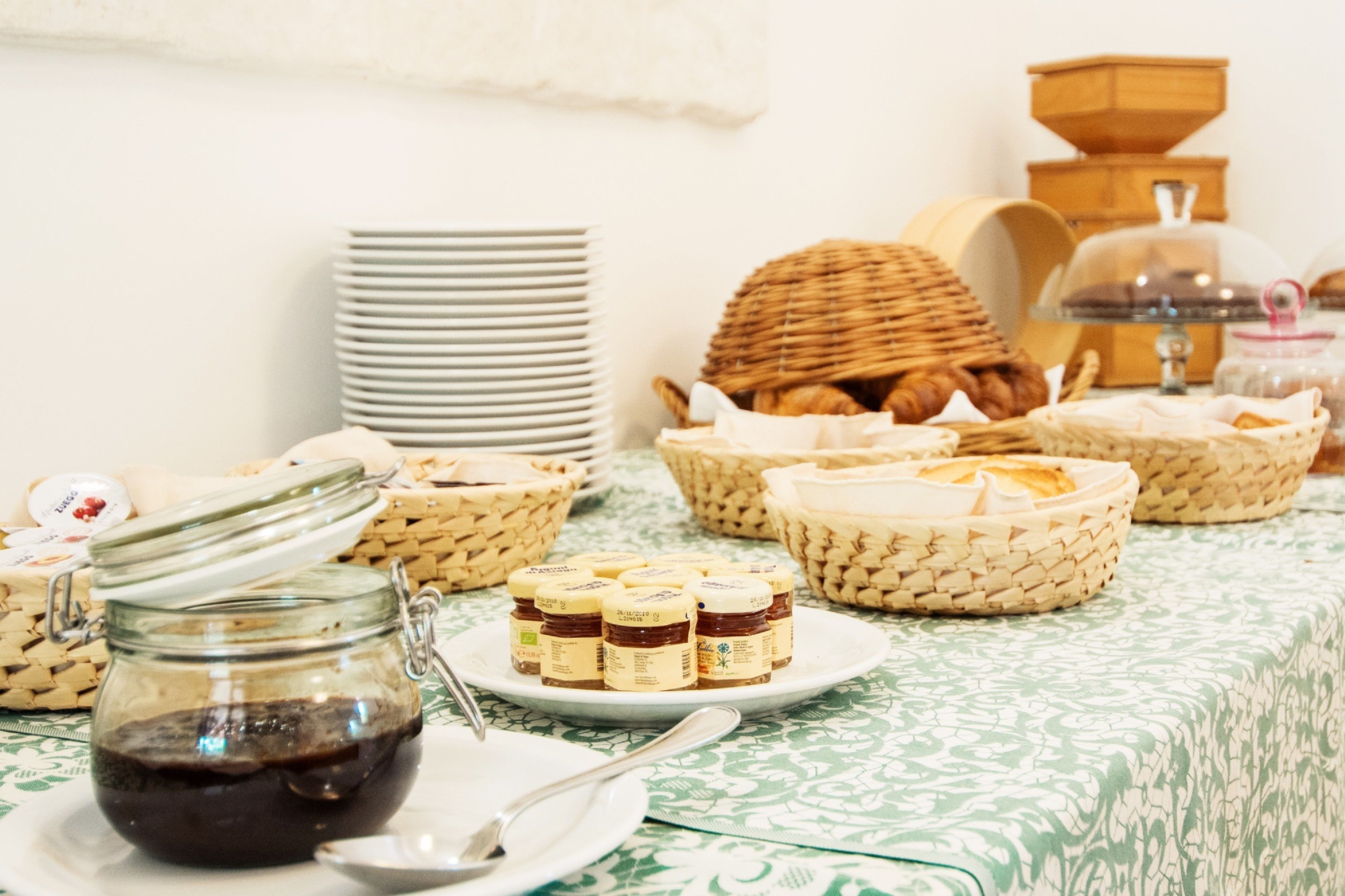 A breakfast buffet with various food items, including jars of jam, baskets of bread, and stacked plates.