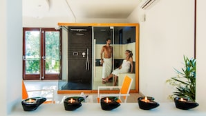 Een moderne spa ruimte met een glazen douchecabine, een witte stoel en kaarsen op de vloer.