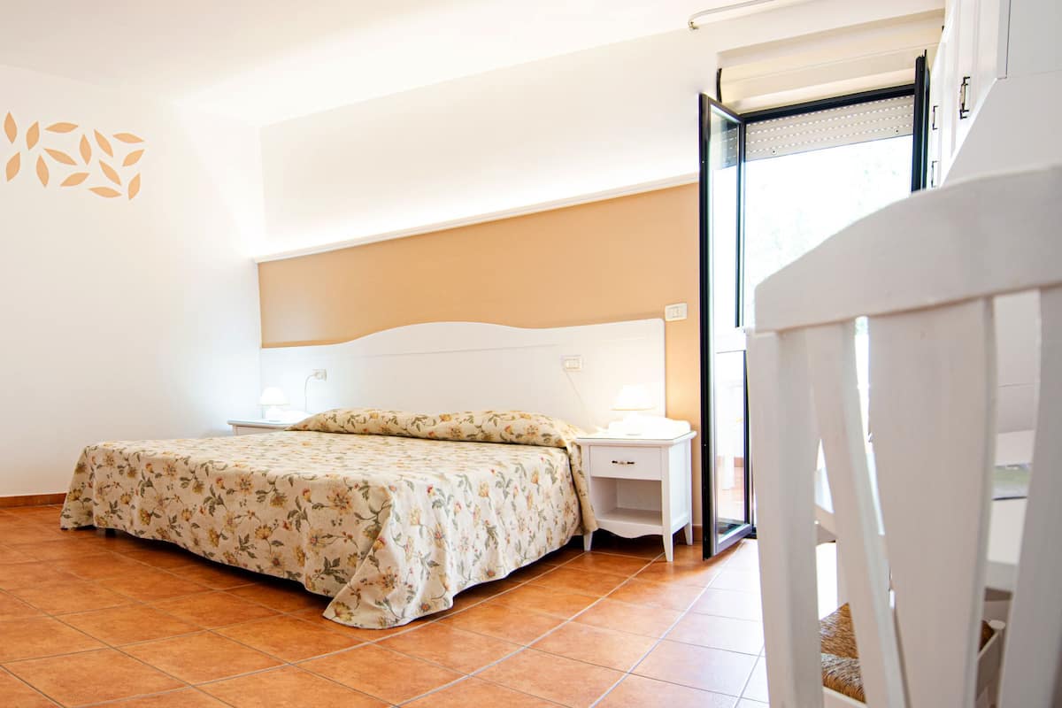 Une chambre à coucher avec un lit, une table de chevet, une commode et une salle de bain visible à travers une porte ouverte.