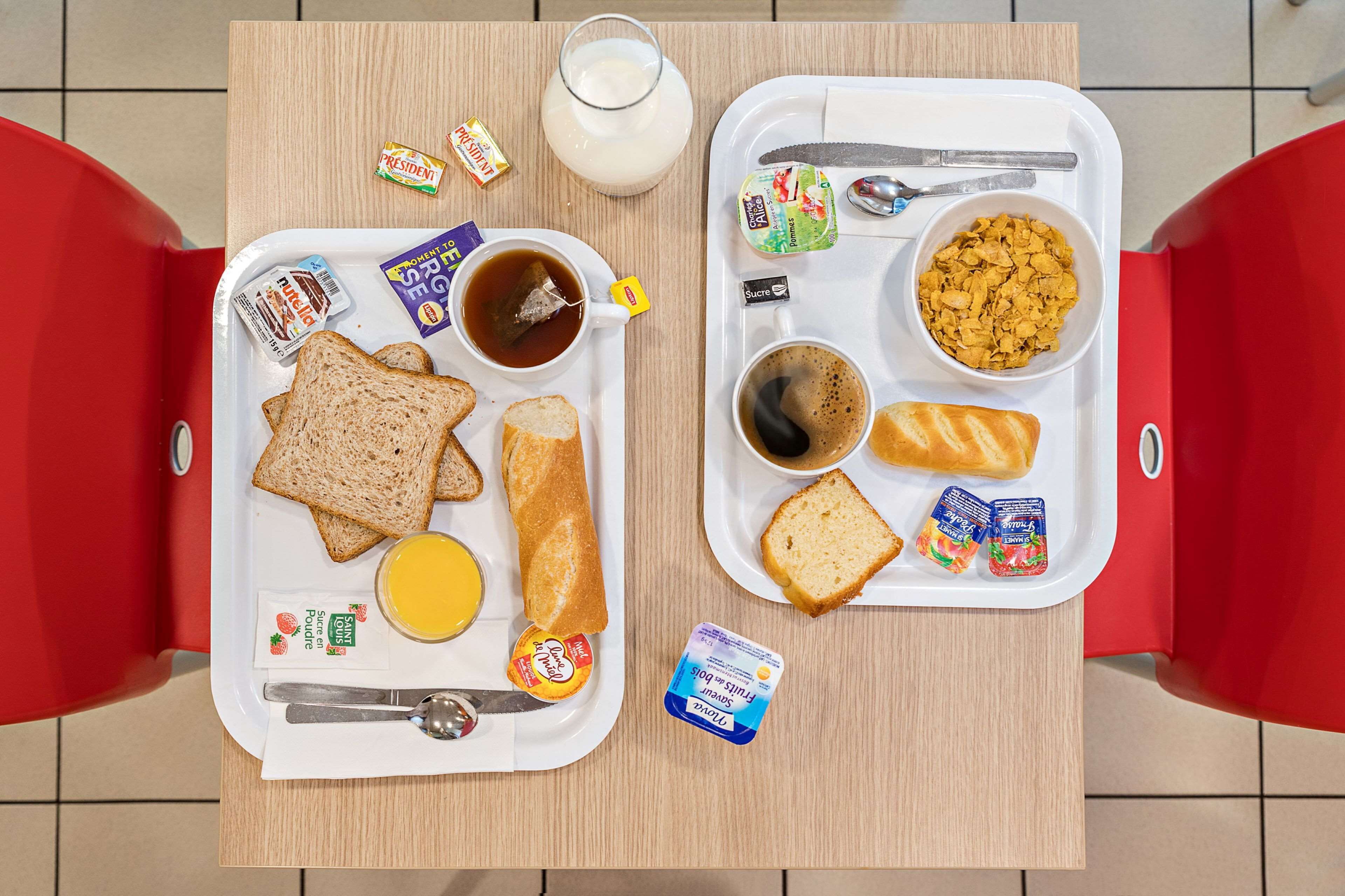 A breakfast tray with toast, butter, jam, a cup of tea, a glass of milk, and yogurt on a wooden table.