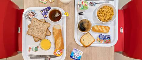A breakfast tray with toast, butter, jam, a cup of tea, a glass of milk, and yogurt on a wooden table.