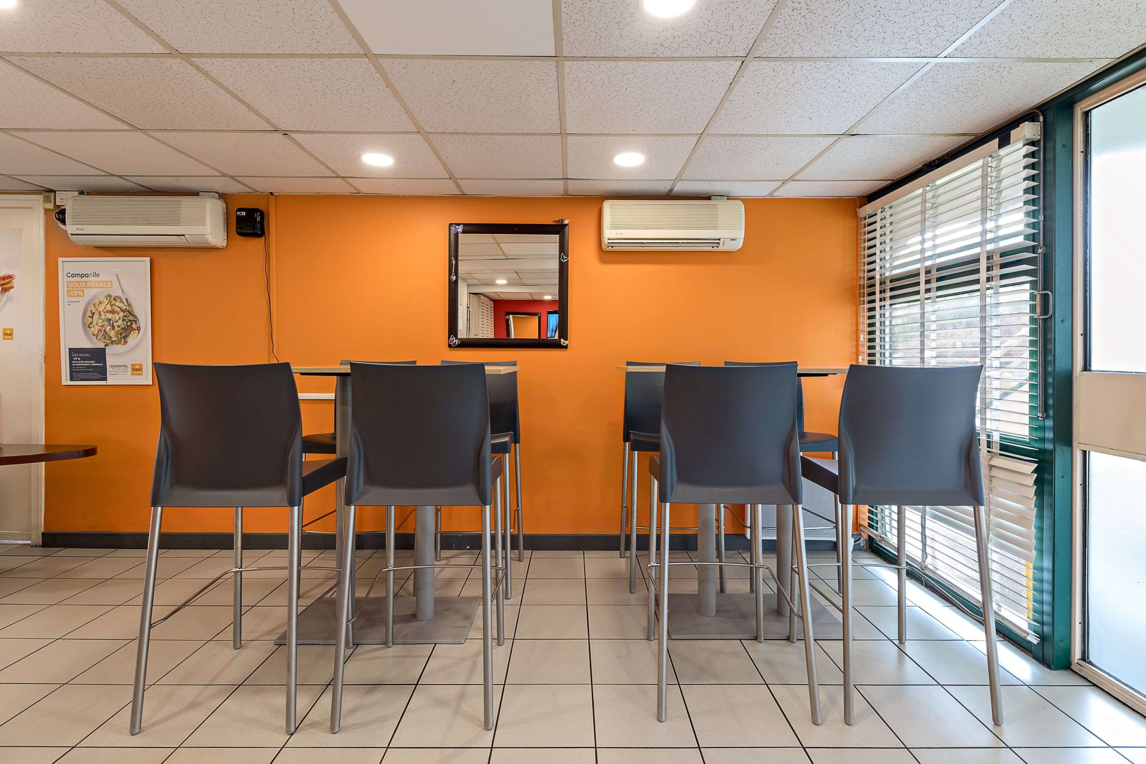 Ein Restaurantinnenraum mit vier schwarzen Stühlen, orangefarbenen Wänden, einem gefliesten Boden und einer Klimaanlage an der Decke.