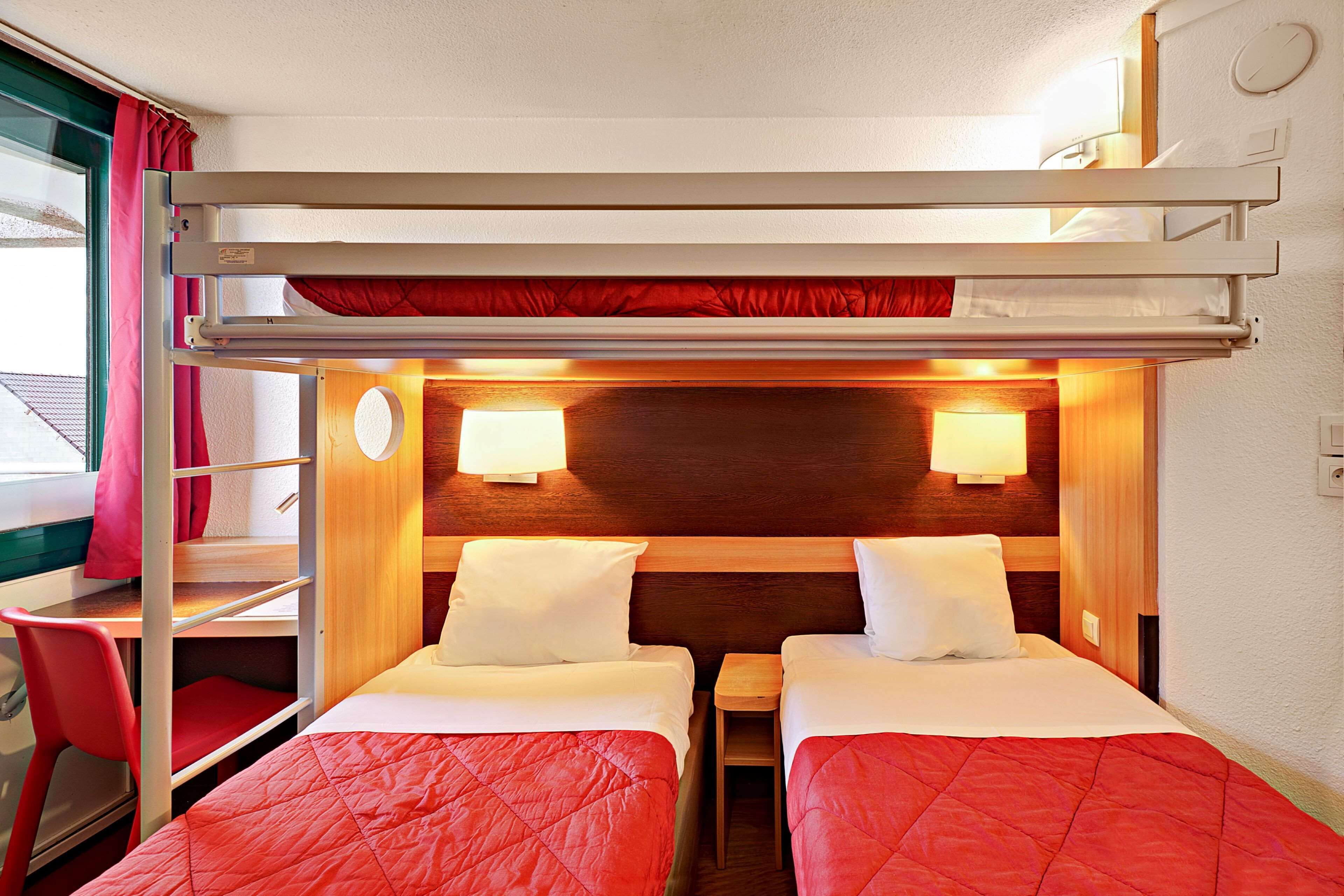 A compact hotel room with bunk beds, a desk, and two bedside tables.