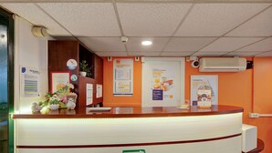 Un comptoir d’accueil avec une pancarte indiquant la direction à suivre vers la droite, une caméra de surveillance et un climatiseur fixé au mur.