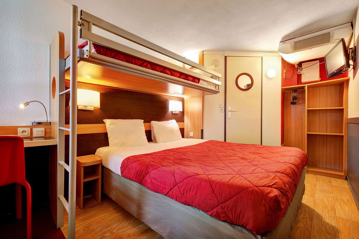 A compact room with a bunk bed, a desk with a chair, a wardrobe, and a television.