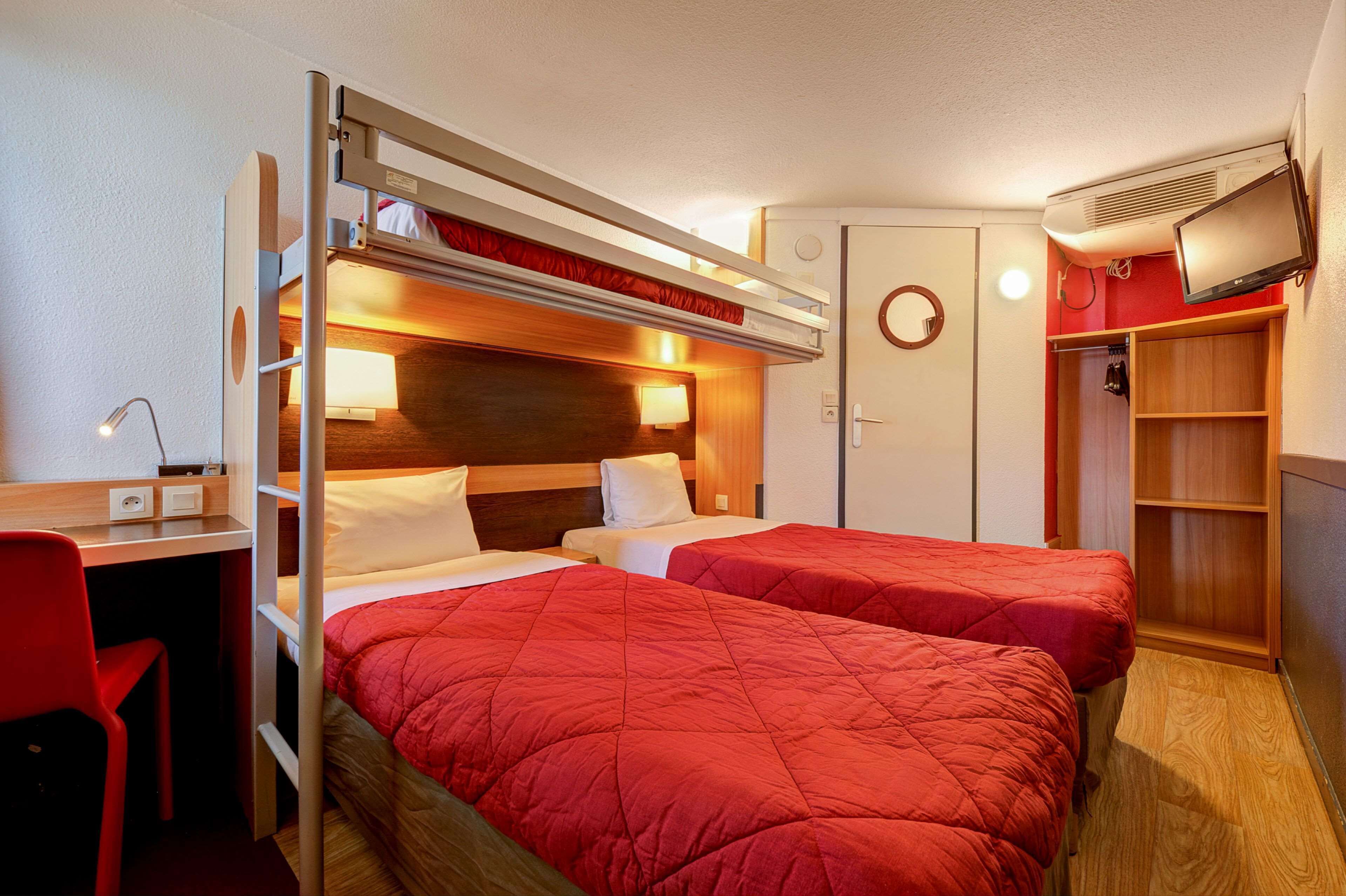 A compact hotel room with two beds, a desk, and a TV.