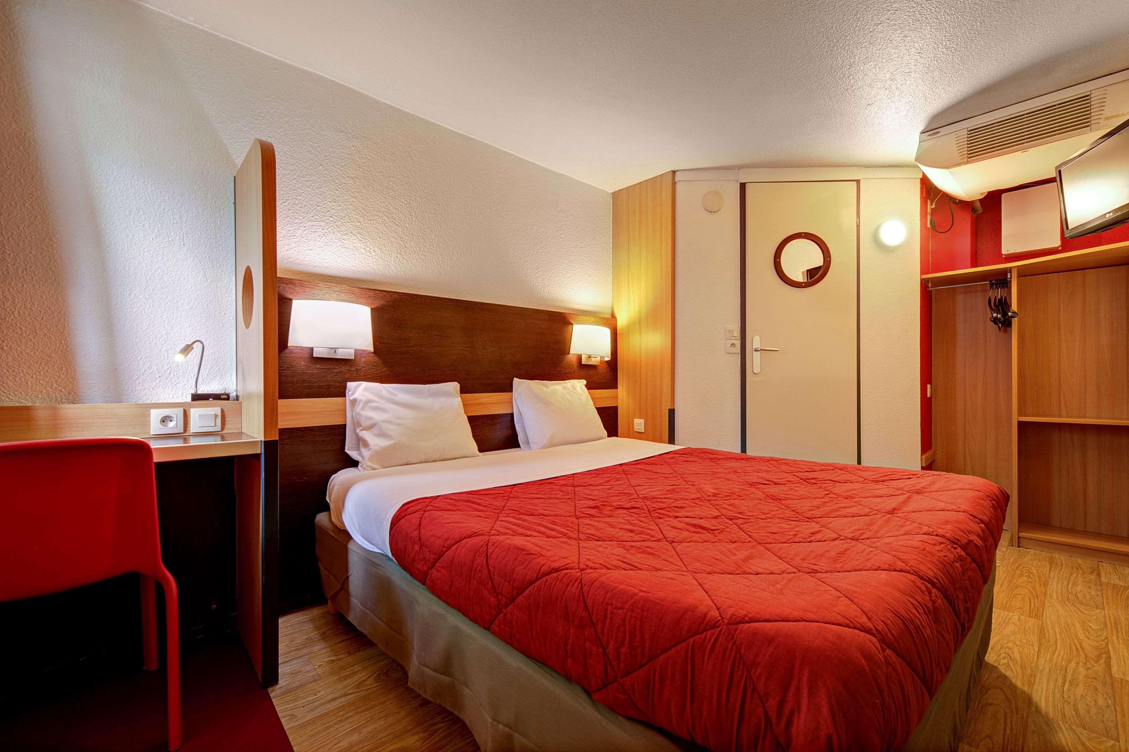 Una habitación de hotel con cama, escritorio, silla, armario y espejo.