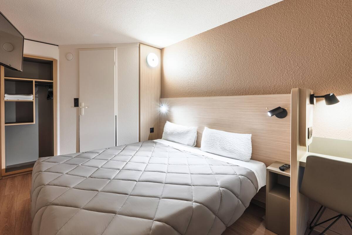 Un dormitorio con cama, escritorio, silla, armario y televisor.