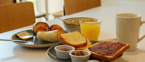 Comida para el desayuno en una mesa, incluyendo tostadas, croissants y una taza.