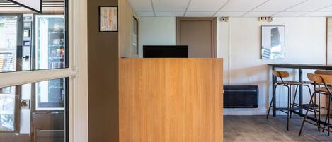 Un espace de bureau moderne avec un comptoir d’accueil en bois, un coin bar avec des tabourets et une grande fenêtre donnant sur la ville.