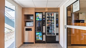 Espaço com máquinas automáticas, incluindo um micro-ondas, um dispensador de bebidas e uma máquina de venda de snacks.