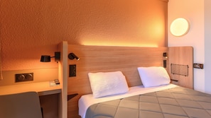 Una habitación de hotel moderna con cabecera de madera, lámparas de noche, un escritorio y una cama con cabecera acolchada.