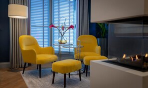 A modern living room with two yellow armchairs, a small round table, a vase with flowers, and a fireplace.