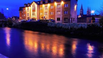 Un hôtel à plusieurs étages, avec une enseigne indiquant « Lancaster Lodge », et dont le reflet se mire dans l’eau.