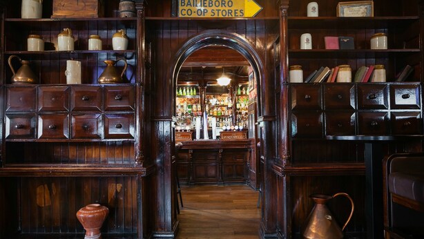 A wooden interior with shelves of jars and bottles, a sign for Bailieboro Co-op Stores, and a wooden counter with a cash register.