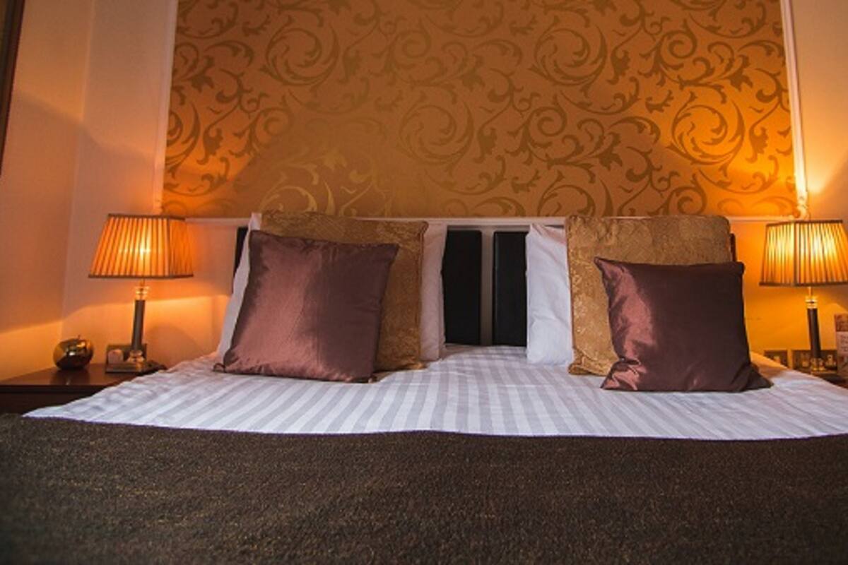 A hotel room with a large bed, two bedside lamps, and a patterned wallpaper.