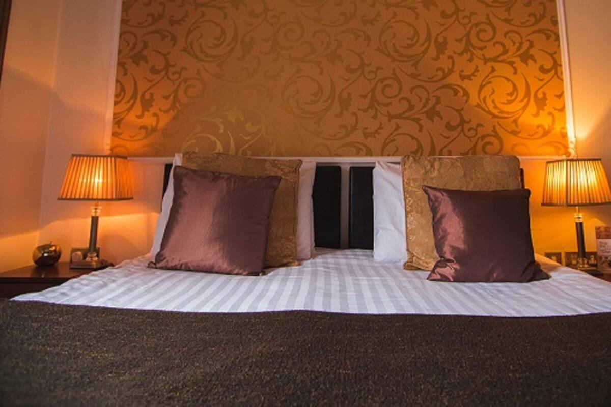 A neatly made bed with two pillows, a striped bedspread, and two bedside lamps on either side.