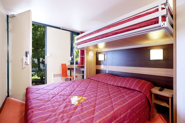 A room with a bunk bed, a desk with a chair, a small table, and a window with a view of greenery. - Première Classe Chateauroux - Saint Maur (Saint-Maur)
