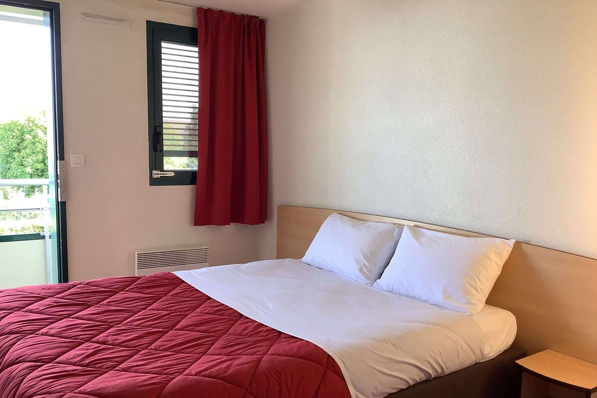 Ein Hotelzimmer mit einem Bett, einem Fenster mit rotem Vorhang und einem kleinen Nachttisch.