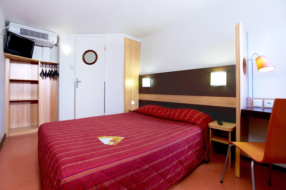 Ein Hotelzimmer mit einem Bett, einem Schreibtisch, einem Stuhl, einem Kleiderschrank und einem Fernseher.