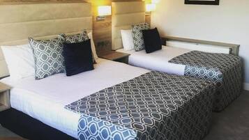 A hotel room with two beds, each with patterned bedding and pillows, a wooden headboard, bedside lamps, and a framed picture on the wall.