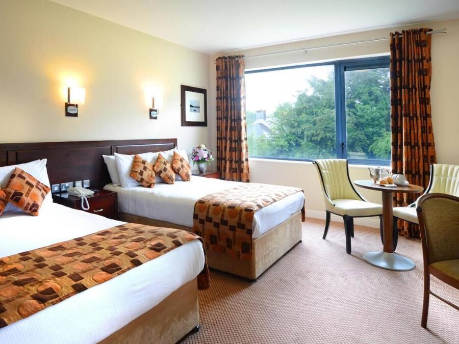 A hotel room with two beds, a small table with chairs, and a window with curtains.