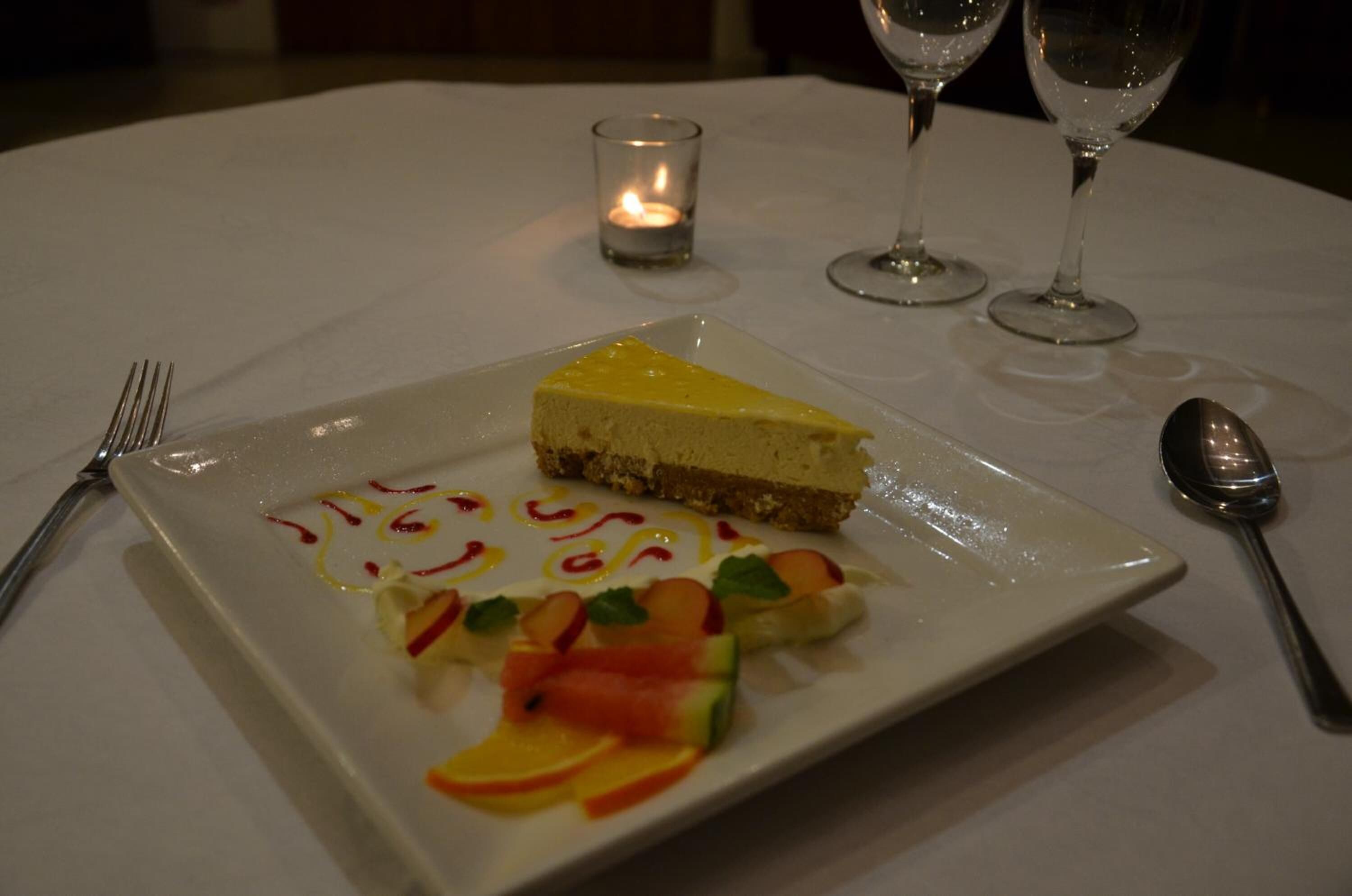Un plato con rebanada de pastel de queso, decoración de frutas y una vela sobre una mesa.