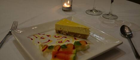 Un plato con rebanada de pastel de queso, decoración de frutas y una vela sobre una mesa.