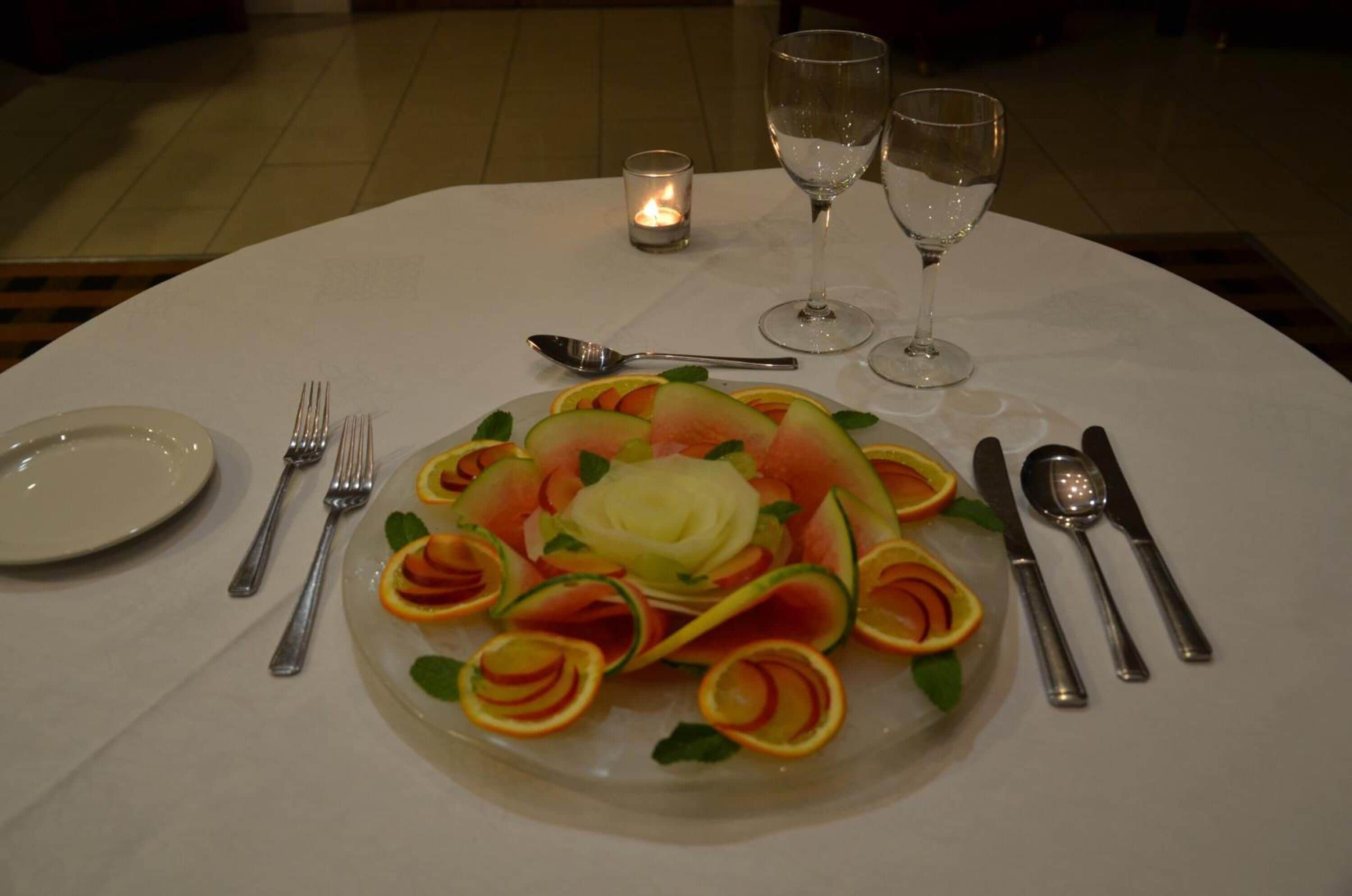 Une table mise pour un repas, agrémentée d’un arrangement de fruits décoratif, de couverts et de verres.