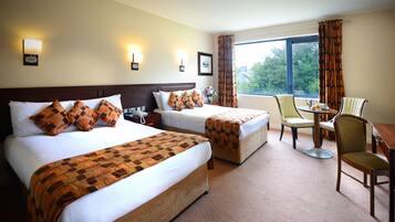 A hotel room with two beds, a desk, a chair, and a view of the outdoors.