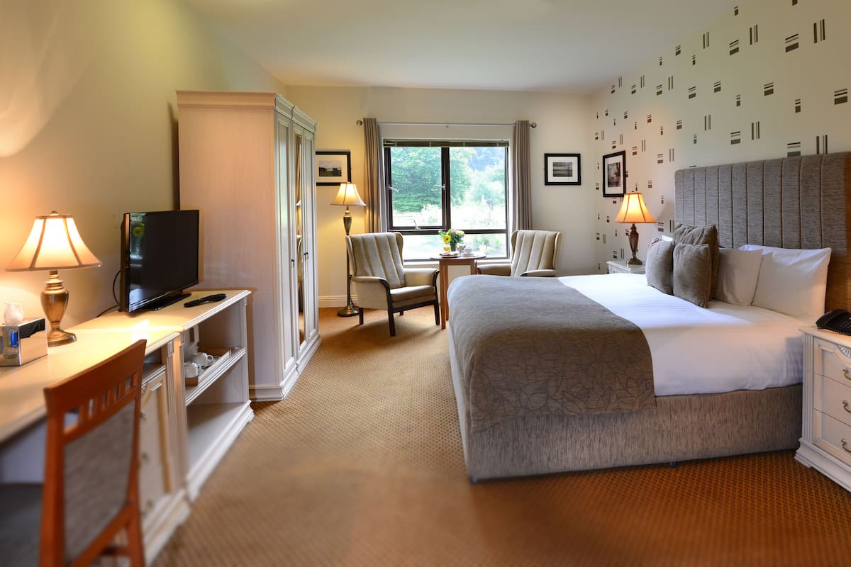 A hotel room with a bed, desk, TV, and chairs.