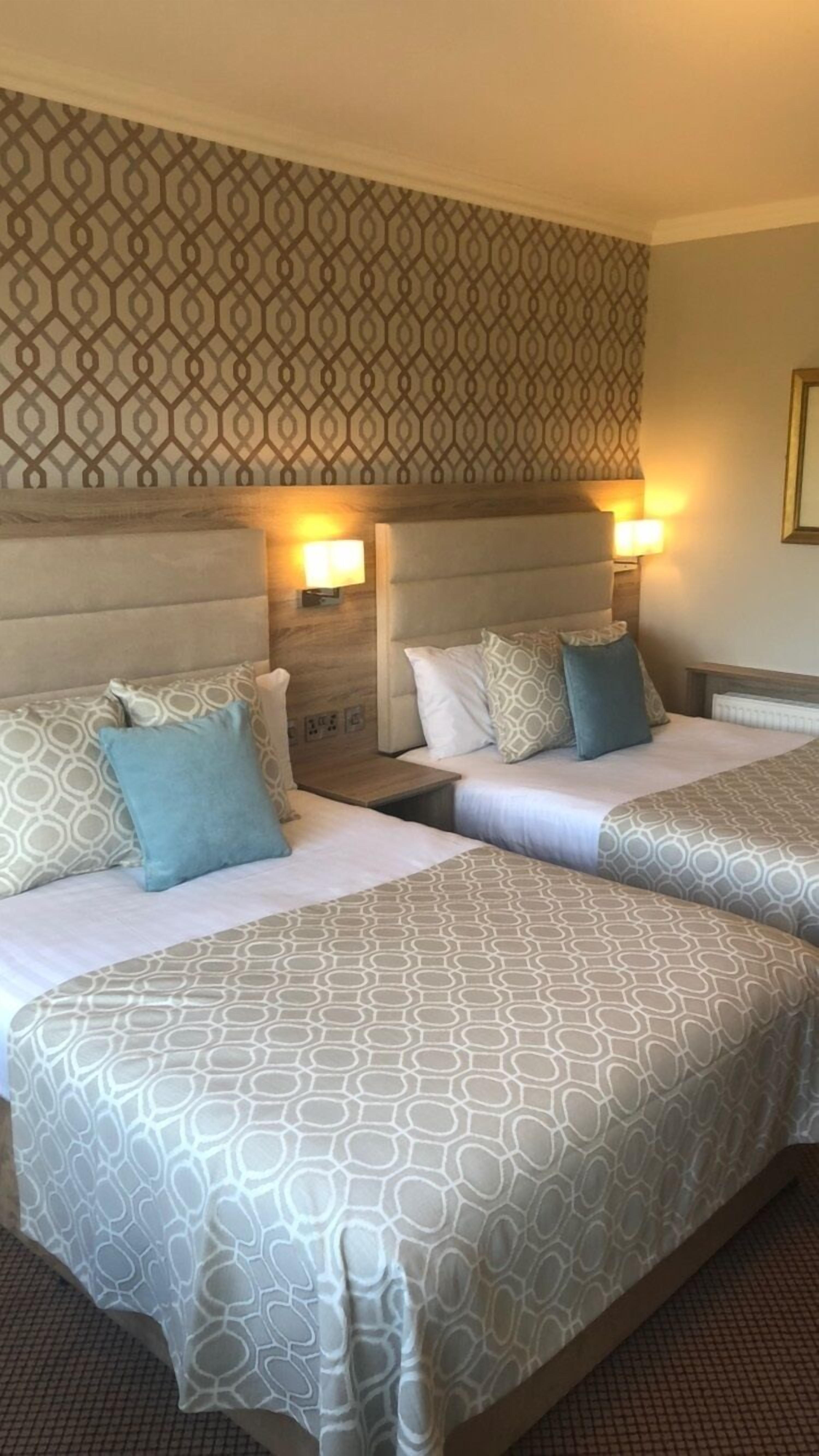 Une chambre d’hôtel avec deux lits, chacun doté de draps à motifs et d’une tête de lit décorée, ainsi que de deux lampes fixées au mur.