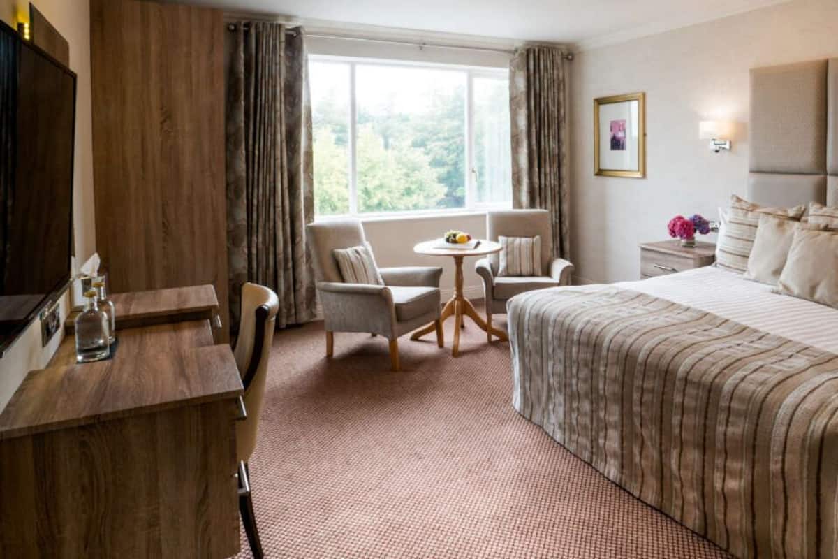 A hotel room with a large bed, a desk, a chair, a small table, and a window with curtains.