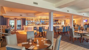 Un moderno vestíbulo de hotel con zona de bar, mesas de comedor y asientos cómodos.