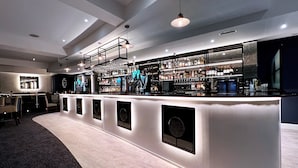 Zona de bar moderna con una barra curva, varios taburetes y una variedad de botellas de licor.