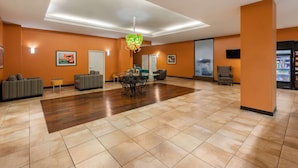 A spacious lobby with a wooden floor, sofas, a dining table, and a decorative hanging light fixture.