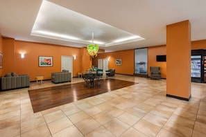 Een ruime lobby met een houten vloer, banken, een eettafel en een decoratieve hanglamp.