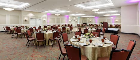 A large banquet hall with multiple round tables, chairs, and a stage.