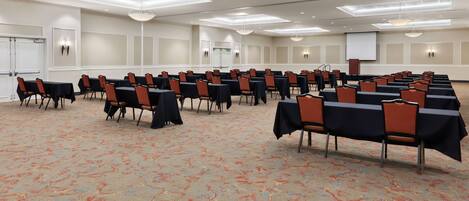 A conference room with rows of tables and chairs, a projector screen, and a whiteboard.