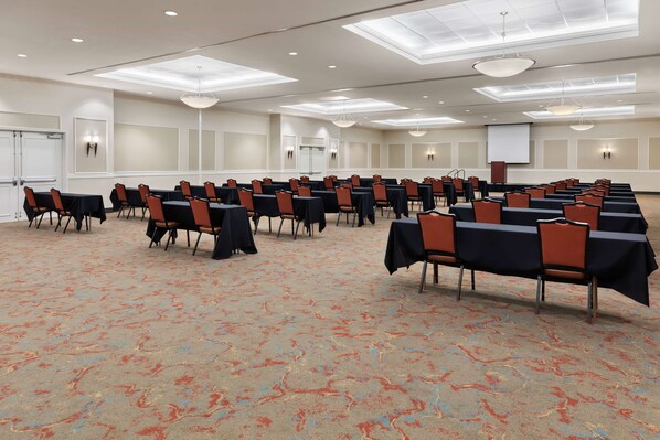 Un salón de conferencias con filas de mesas y sillas, una pantalla de proyector y una pizarra.