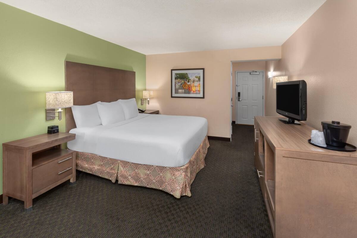 Ein Hotelzimmer mit Bett, Fernseher, Schreibtisch, Lampe, Nachttisch und Tür.