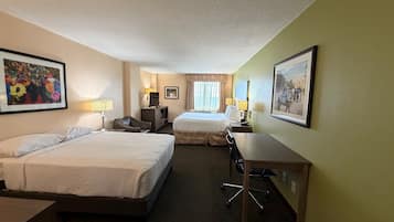 A hotel room with two beds, a desk, a chair, a TV, and a desk lamp.