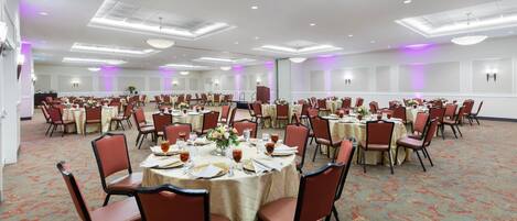 Un amplio salón de banquetes con mesas redondas, sillas y piso alfombrado.