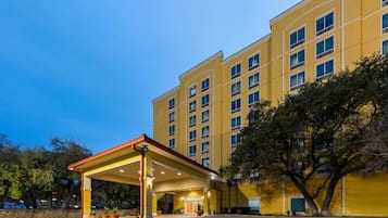 Un hotel con entrada cubierta, varios pisos y fachada amarilla.