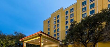 A hotel with a covered entrance, multiple floors, and a yellow facade.