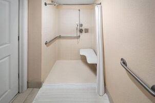 A bathroom with a shower, grab bars, and a white sink.