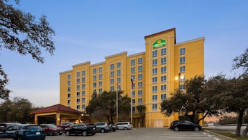 Um hotel com fachada amarela, vários andares e um estacionamento com diversos carros.