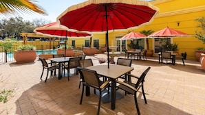 An outdoor patio area with tables and chairs, red umbrellas, and potted plants. - La Quinta Inn & Suites by Wyndham San Antonio Medical Ctr NW (San Antonio)