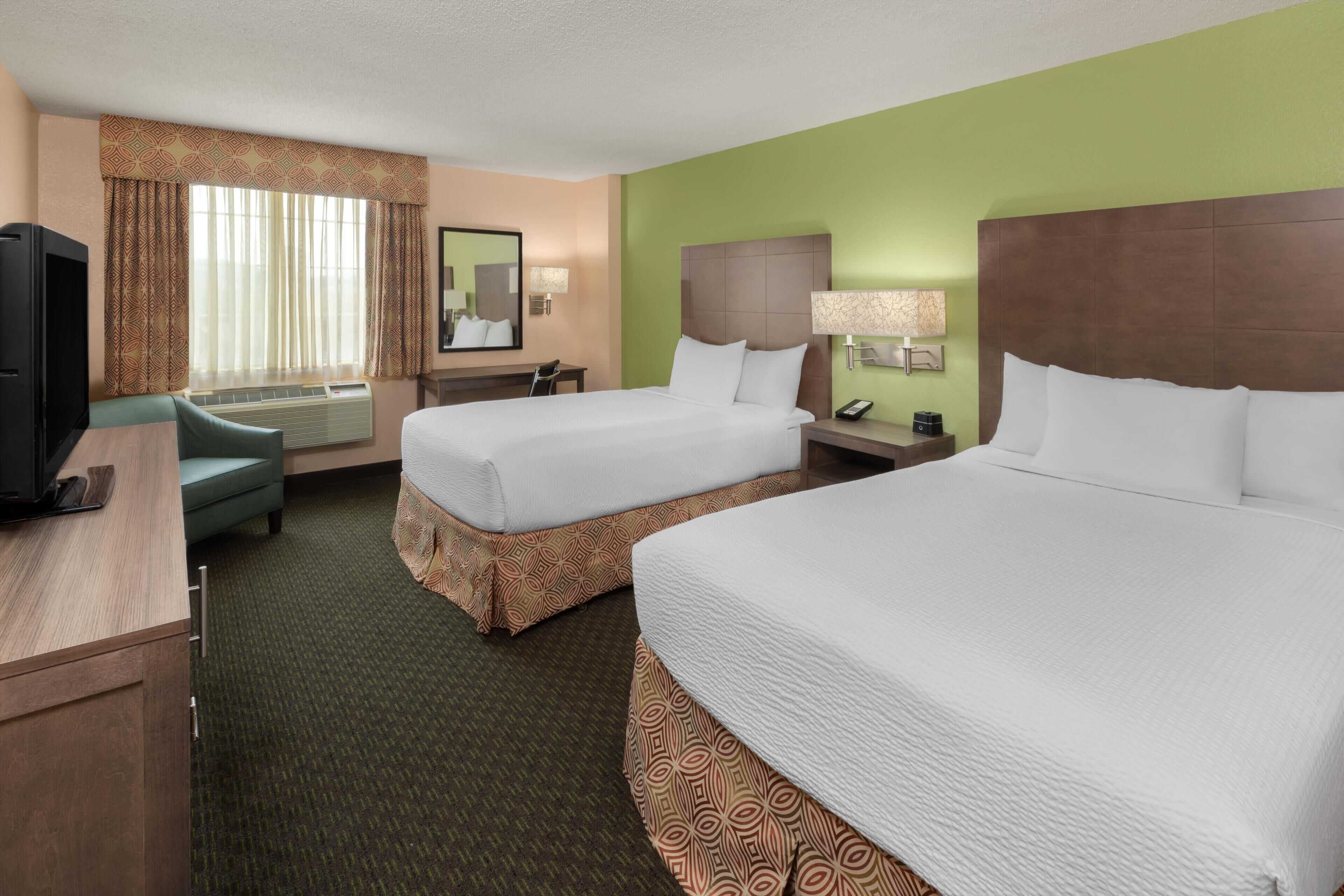A hotel room with two beds, a desk, a TV, a chair, and a mirror.