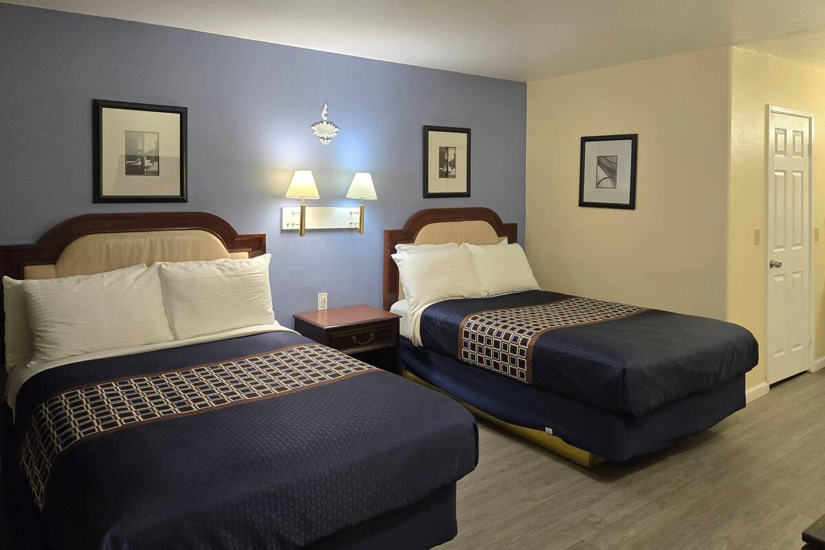 A hotel room with two beds, a nightstand, a lamp, and a door.